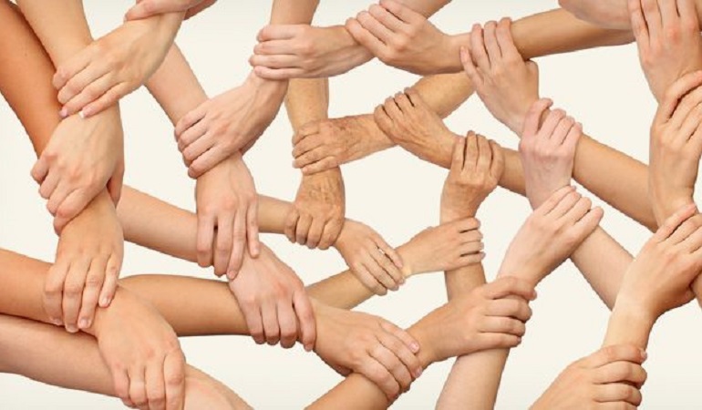Allemaal armen waarvan de handen elkaars polsen vastpakken, symbool voor samenwerken, bij nieuwsbericht over BIZ